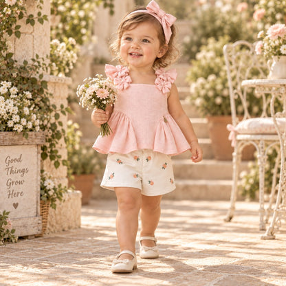 Conjunto de blusa rosa con moños y short blanco con flores bordadas sobre fondo beige
