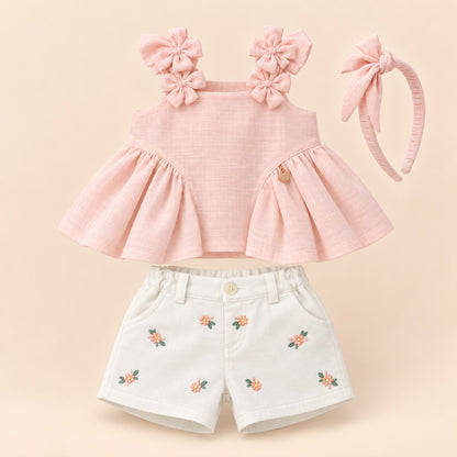 Vista posterior de la blusa rosa con vuelo, short blanco bordado y moño para el cabello