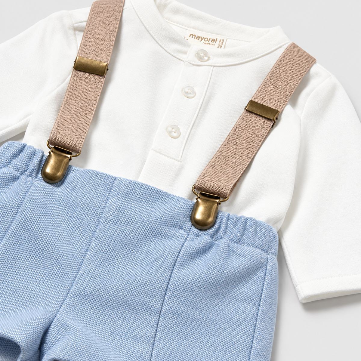 Vista posterior del conjunto de pantalón corto azul claro con tirantes y camisa blanca para bebé