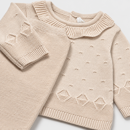 Detalle de jersey tricot beige con cuello de volantes y pantalón tejido para recién nacida