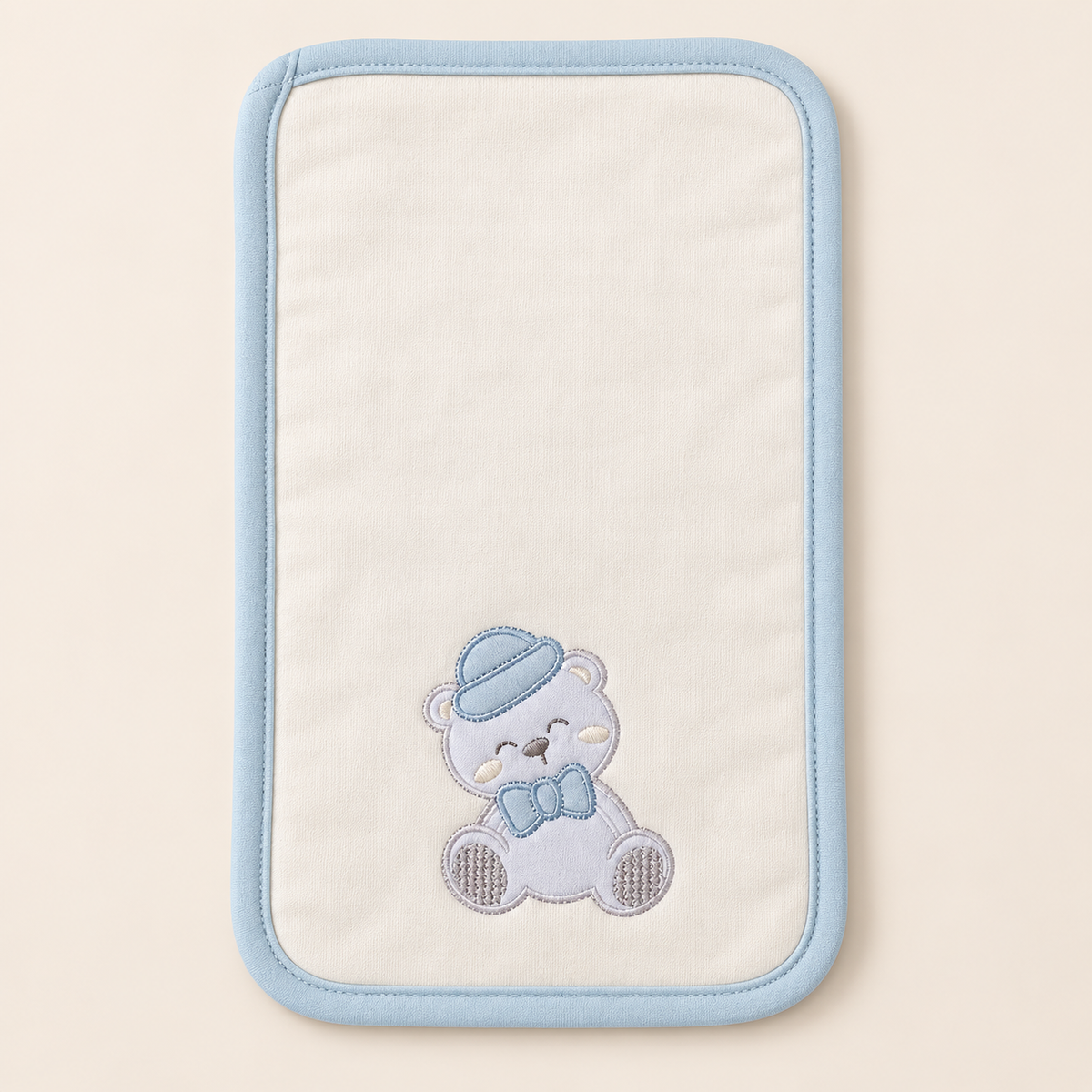 Babero tipo pañito crema con bordes azules y osito bordado