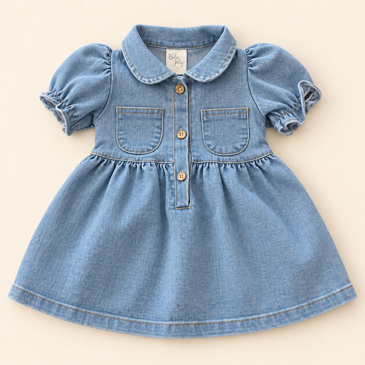 Detalle de vestido denim azul claro para bebé con cuello, bolsillos y botones frontales
