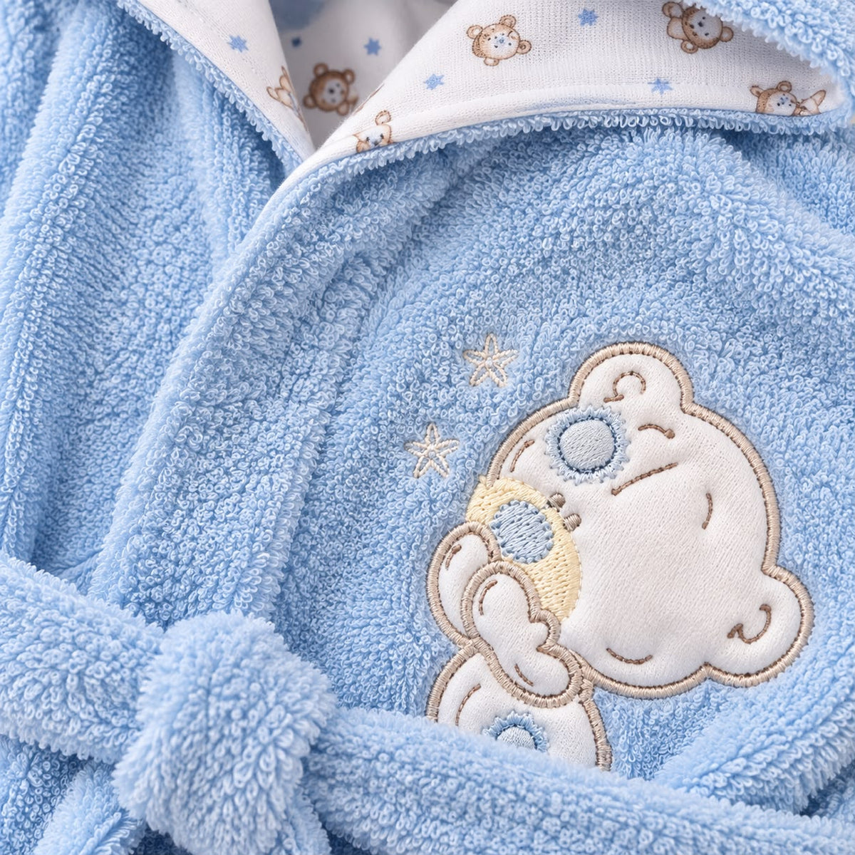 Bebé con bata de baño azul, capucha y osito bordado