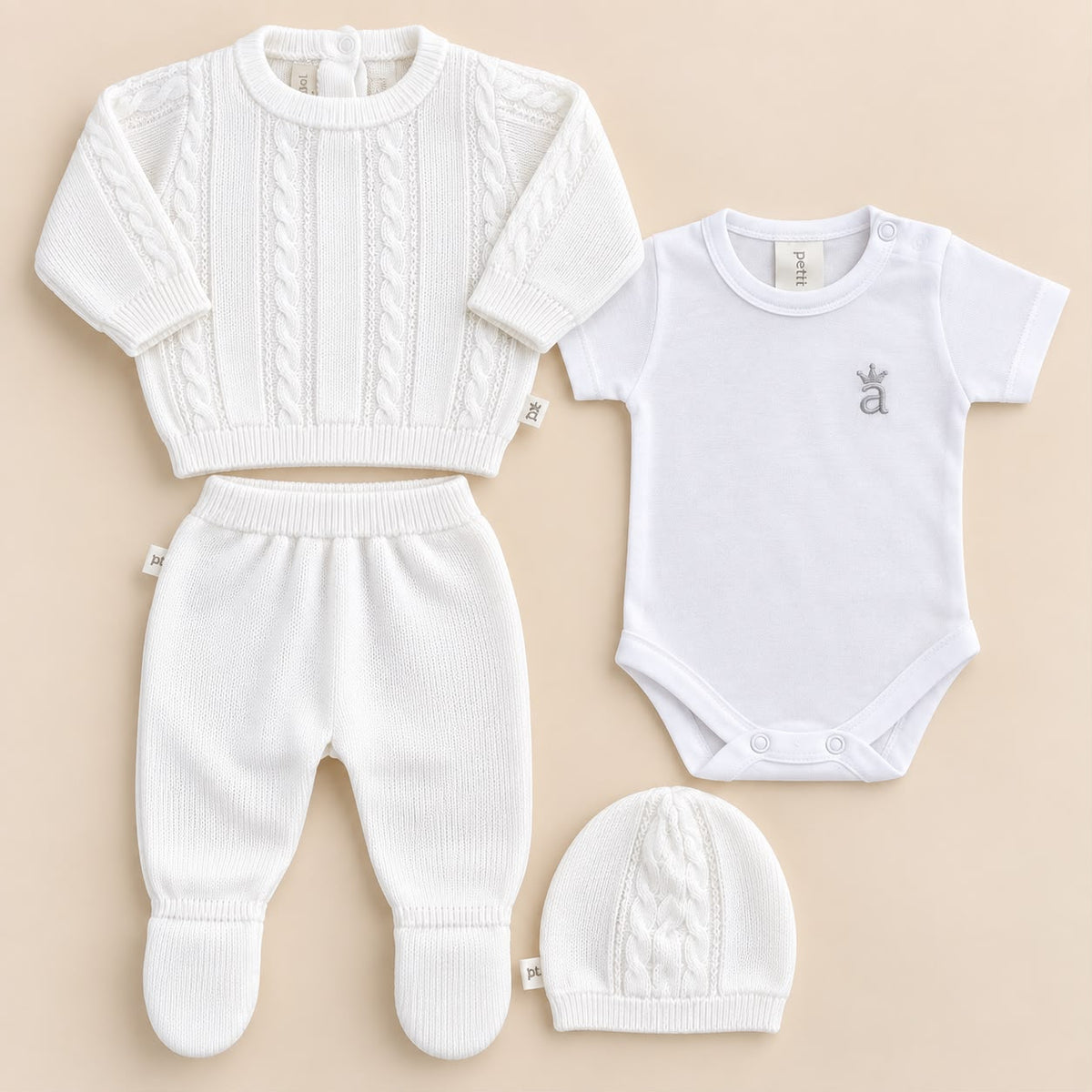 Cuatro piezas del conjunto tejido blanco para bebé extendidas: suéter, pantalón, body y gorro