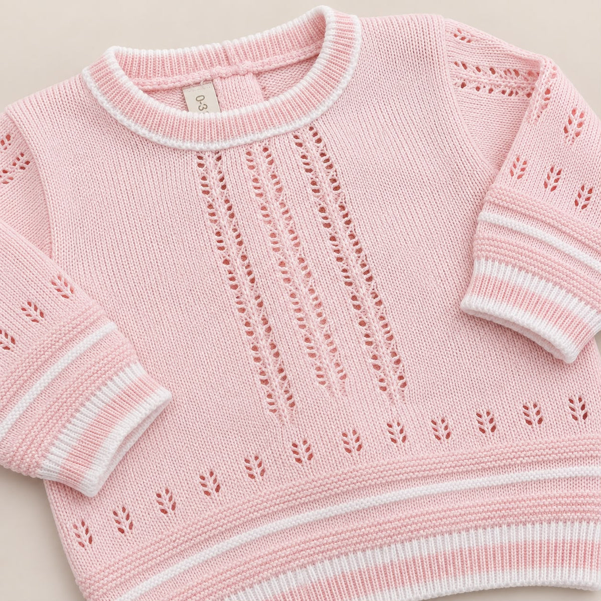 Bebé usando conjunto tejido rosado de cuatro piezas con suéter, pantalón con pie, gorro y body