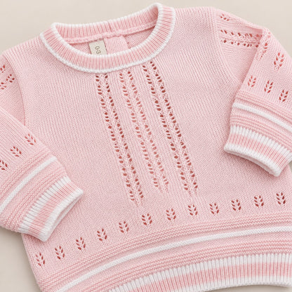 Bebé usando conjunto tejido rosado de cuatro piezas con suéter, pantalón con pie, gorro y body