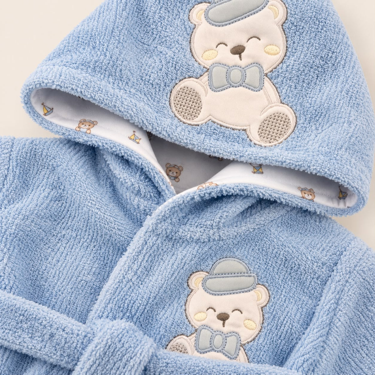 Bebé usando bata de baño azul con capucha y osito con sombrero bordado
