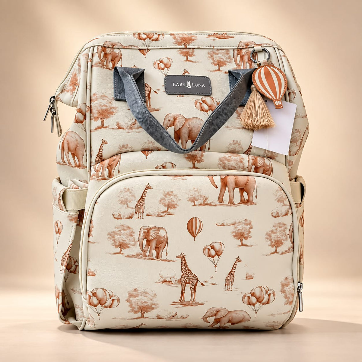 Mochila pañalera Safari Baby Luna en cuero vegano beige con estampado de elefantes y jirafas