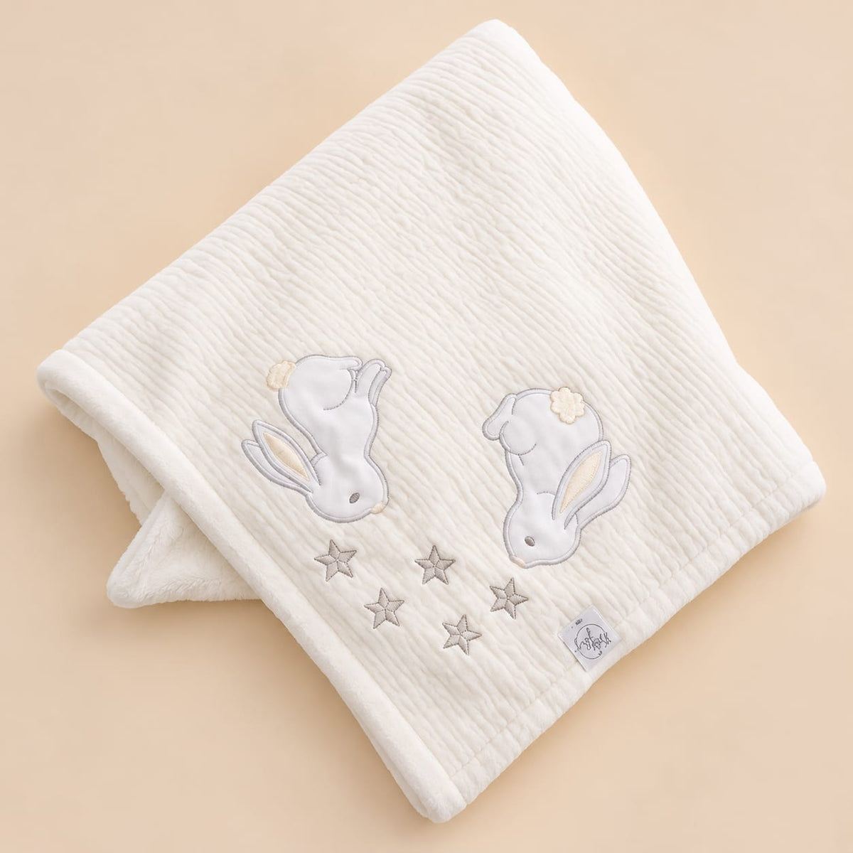 Manta blanca para bebé doblada con detalle de conejitos y estrellas bordados