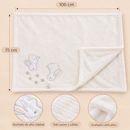 Manta blanca con conejitos bordados y medidas indicadas de 100 por 75 centímetros