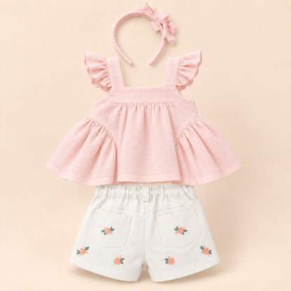 Bebé niña con blusa rosa de moños, short blanco bordado floral y moño rosa para el cabello