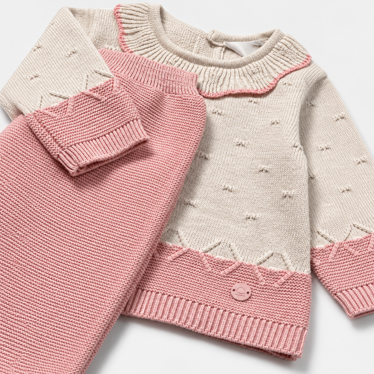 Detalle del jersey crema con cuello de volante y terminaciones rosas junto a la polaina de tricot