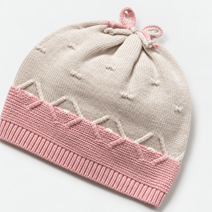 Gorro de tricot para recién nacida en crema con borde rosa y lazo