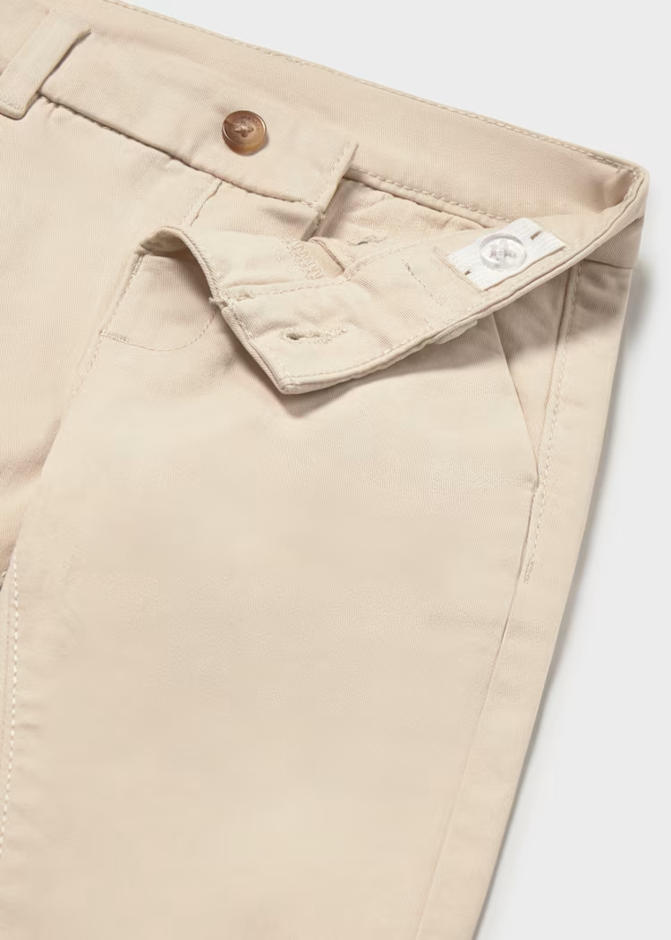 Detalle de cierre con botón y tejido de pantalón chino beige para bebé