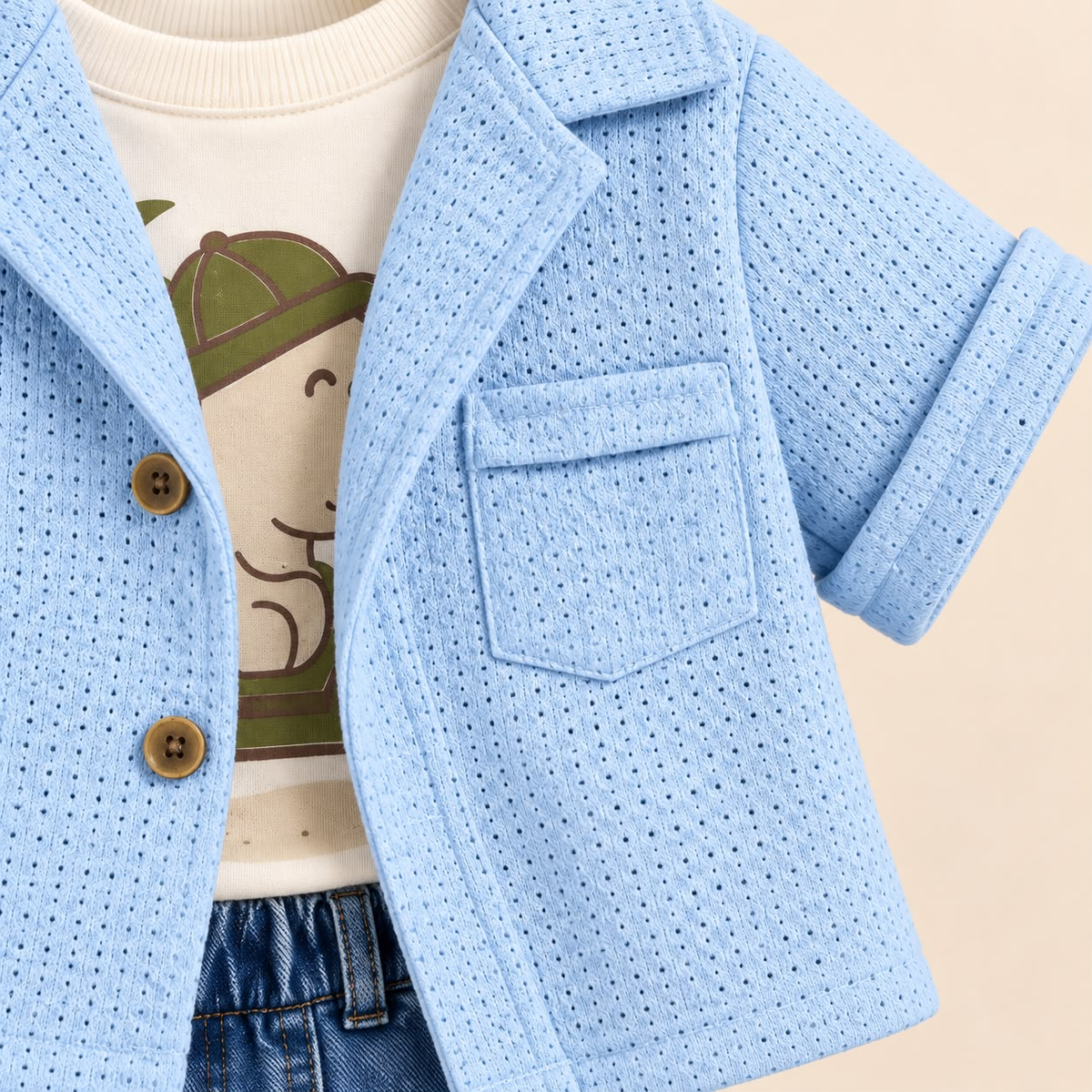 Detalle de chaqueta azul con botones y bolsillo sobre camiseta blanca estampada de dinosaurio