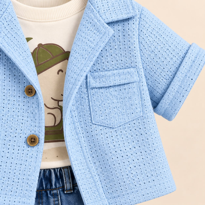 Detalle de chaqueta azul con botones y bolsillo sobre camiseta blanca estampada de dinosaurio