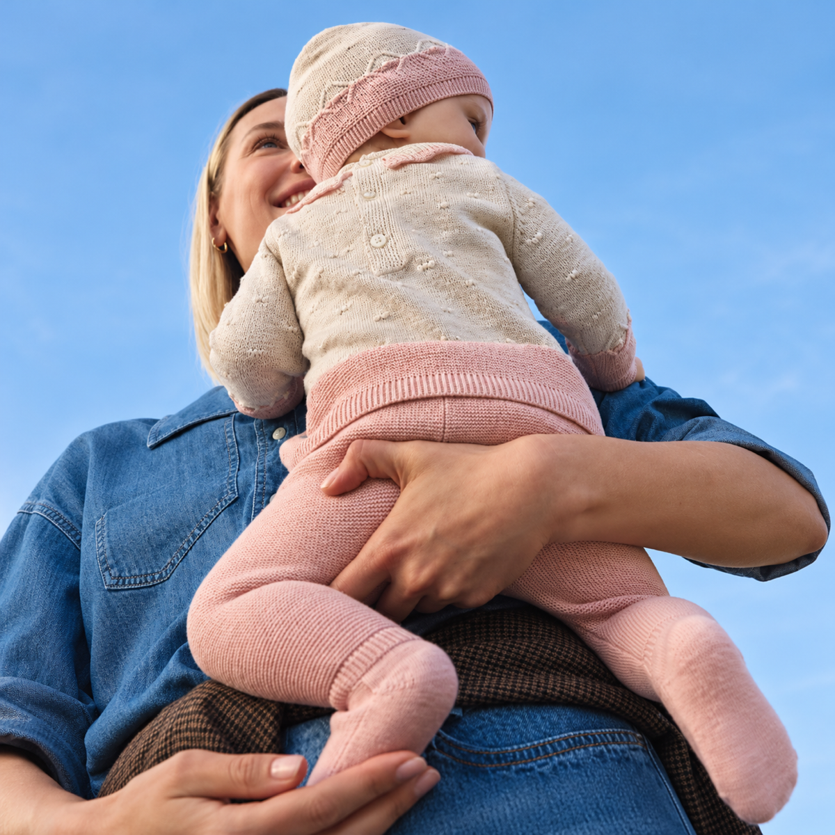 Bebé en brazos de su madre con conjunto de tricot rosa y crema de tres piezas